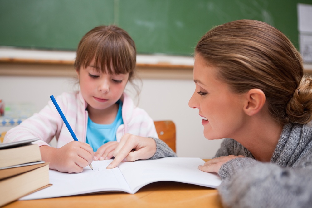 Cute schoolgirl writing a while her teacher is talking in a classroom.jpeg